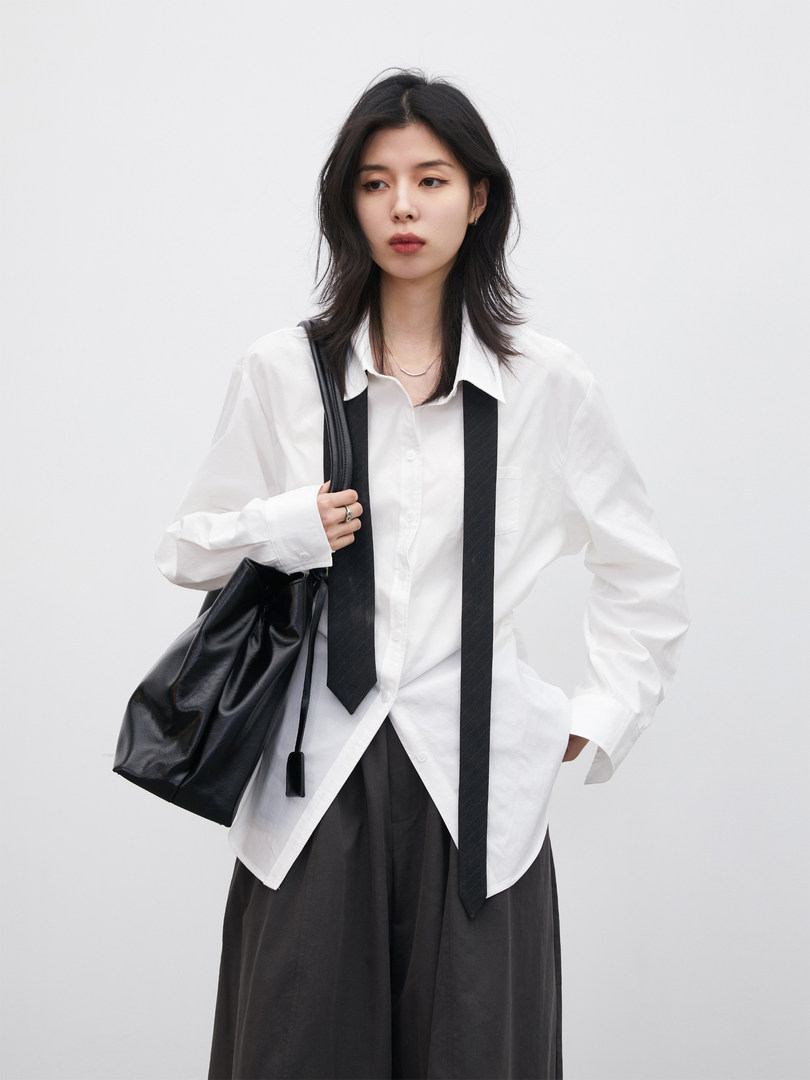 Model wearing a white button-up shirt with a black tie and black shoulder bag