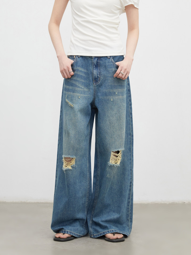 Model wearing distressed wide-leg blue jeans with a white top