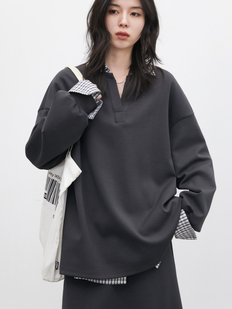 Model wearing a dark oversized long-sleeve top with layered plaid shirt details and matching skirt