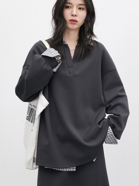 Model wearing a dark oversized long-sleeve top with layered plaid shirt details and matching skirt