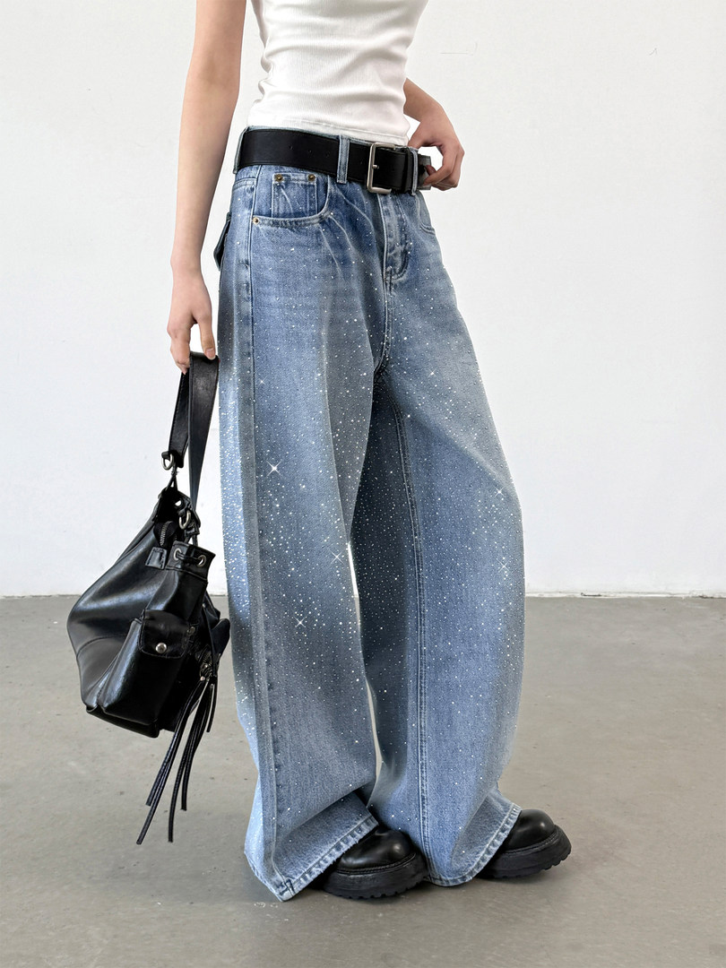 Model wearing wide-leg sparkly blue jeans with a black belt and bag