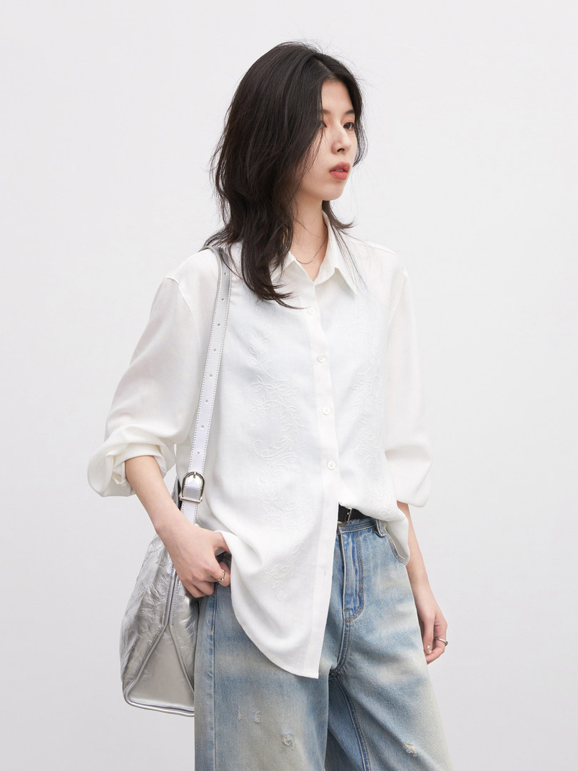 Model wearing a white long-sleeve blouse with light wash jeans and a silver shoulder bag