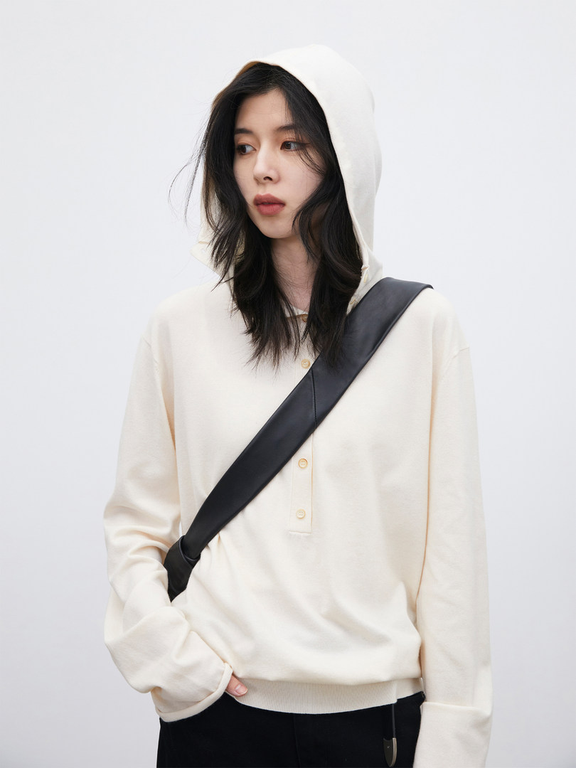 Model wearing a cream hooded sweatshirt with a black crossbody strap