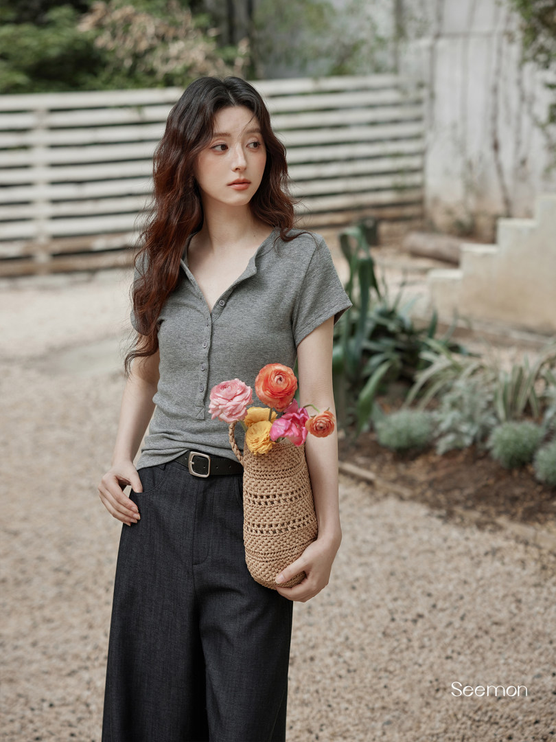Model wearing a gray short-sleeve button-up top with black wide-leg pants and holding a woven basket bag