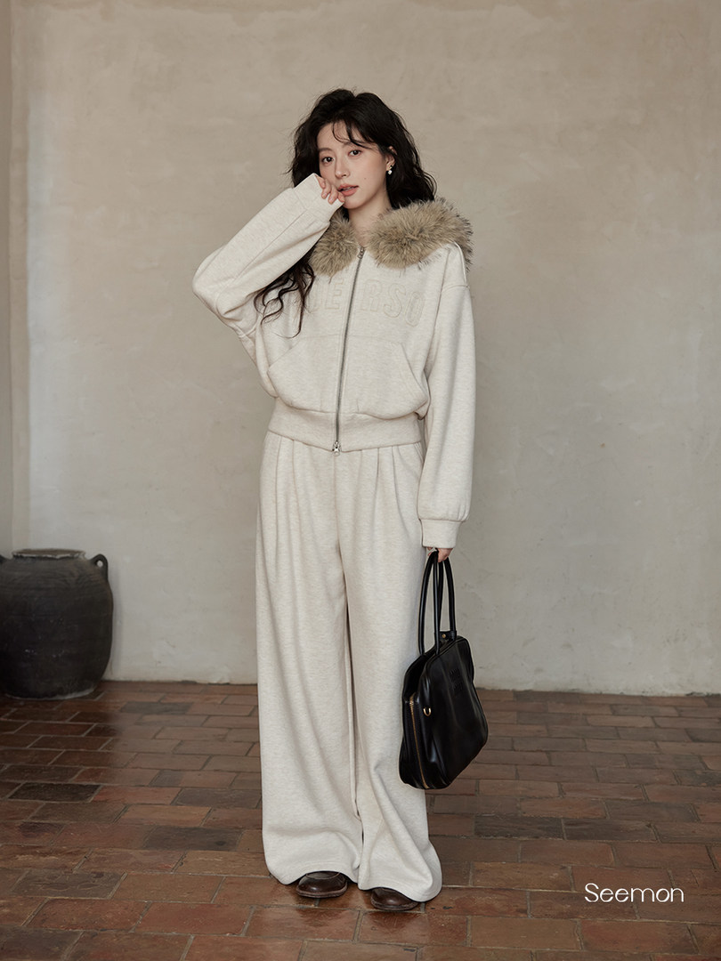 Model wearing a cream zip-up outfit with fur-trim hood and black handbag