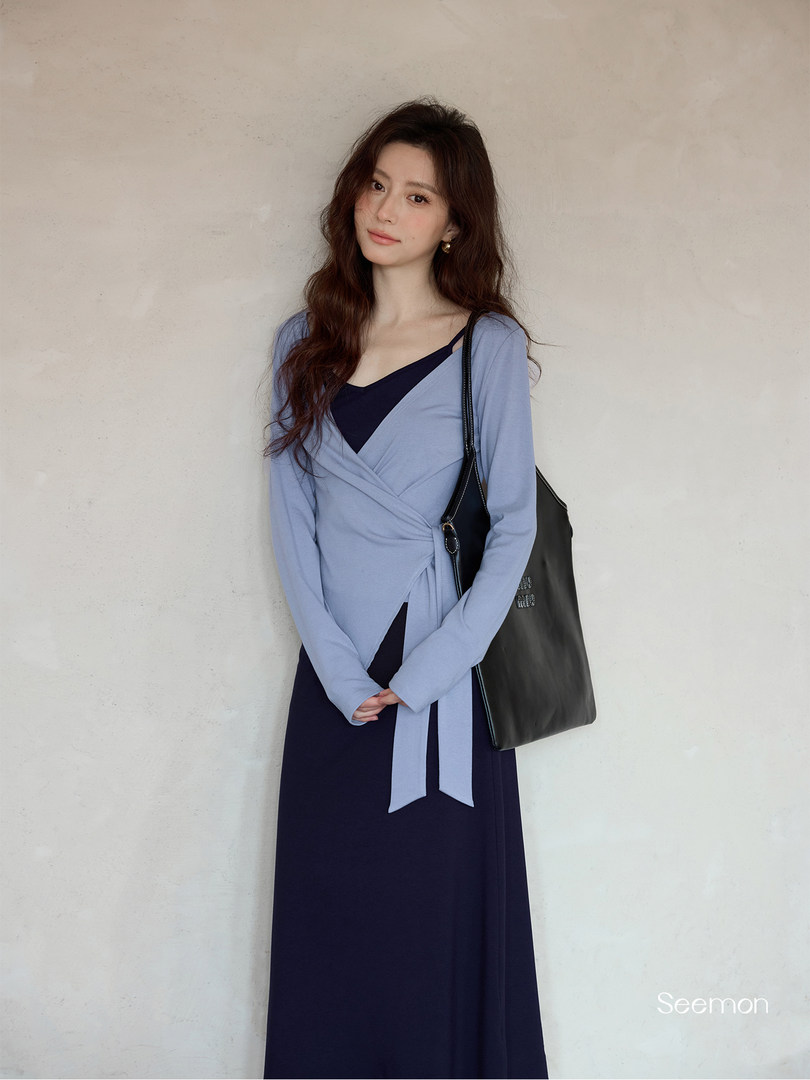 Model wearing a light blue wrap dress over a navy dress with a black shoulder bag