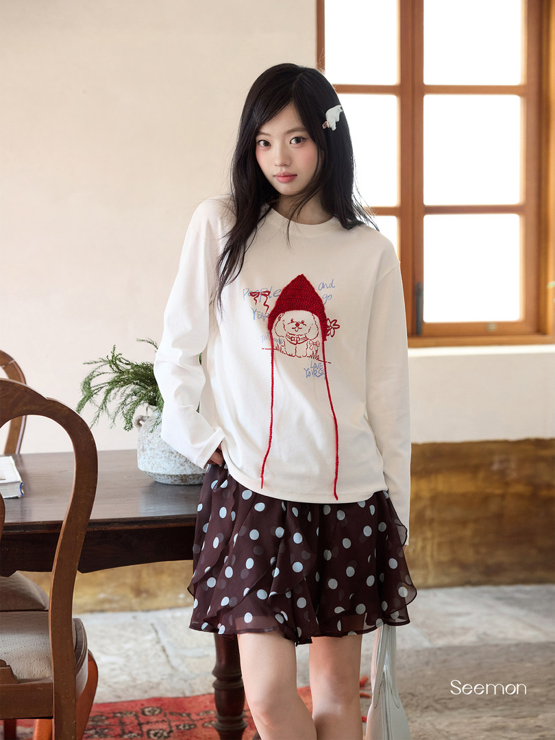 Model wearing a white graphic long-sleeve top and brown polka dot skirt