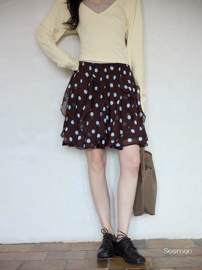 Model wearing a pale yellow long-sleeve top with a brown polka dot skirt and black shoes