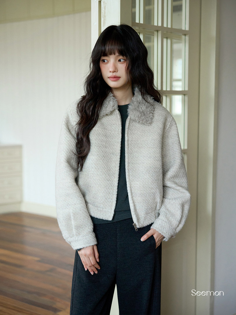 Woman wearing a light gray fuzzy jacket and dark pants indoors