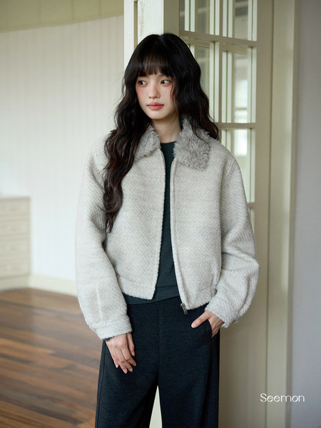 Woman wearing a light gray fuzzy jacket and dark pants indoors