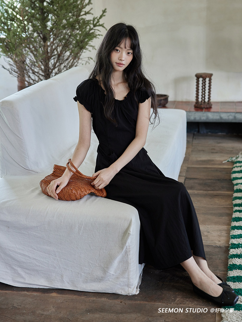 Black midi dress worn by a model seated on a sofa