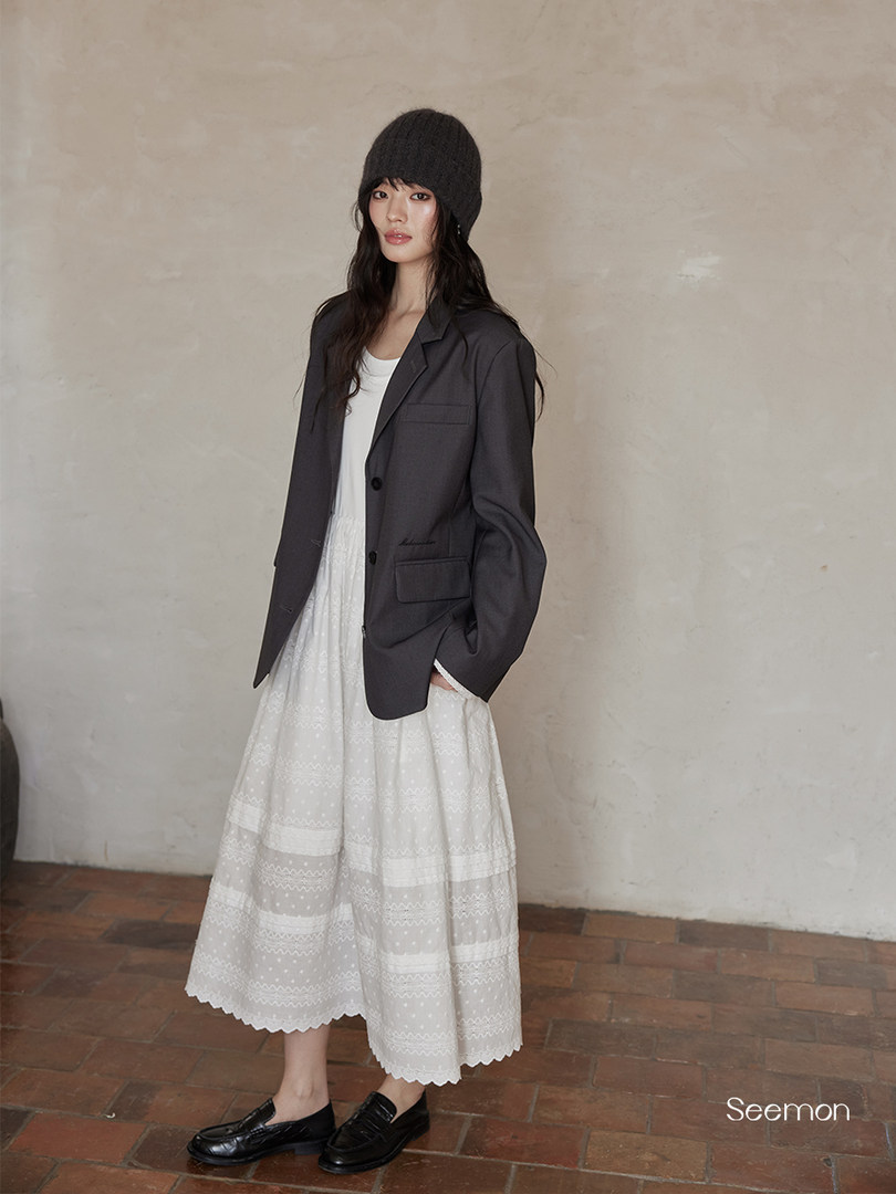 Model wearing a dark blazer over a white dress with a black knit beanie and loafers
