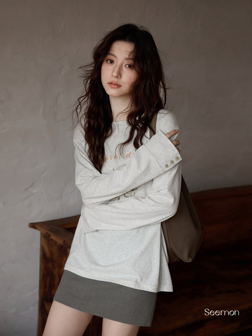 Model wearing a light gray long-sleeve top and gray mini skirt with a shoulder bag