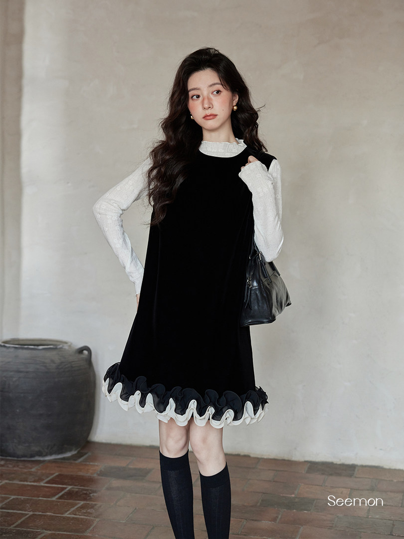 Model wearing a black sleeveless ruffle-hem dress layered over a white long-sleeve top