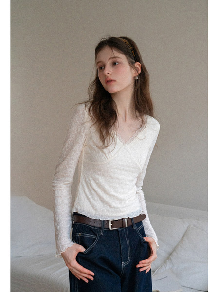Woman wearing a white long-sleeve fitted lace-textured top with dark jeans