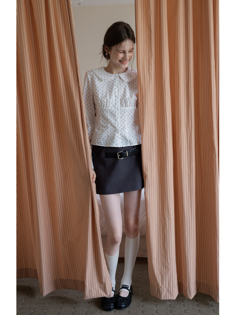 Woman modeling a white polka dot blouse with a black mini skirt and black loafers