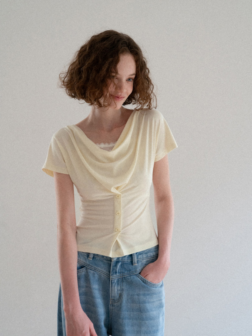 Model wearing a cream draped short-sleeve top with blue jeans