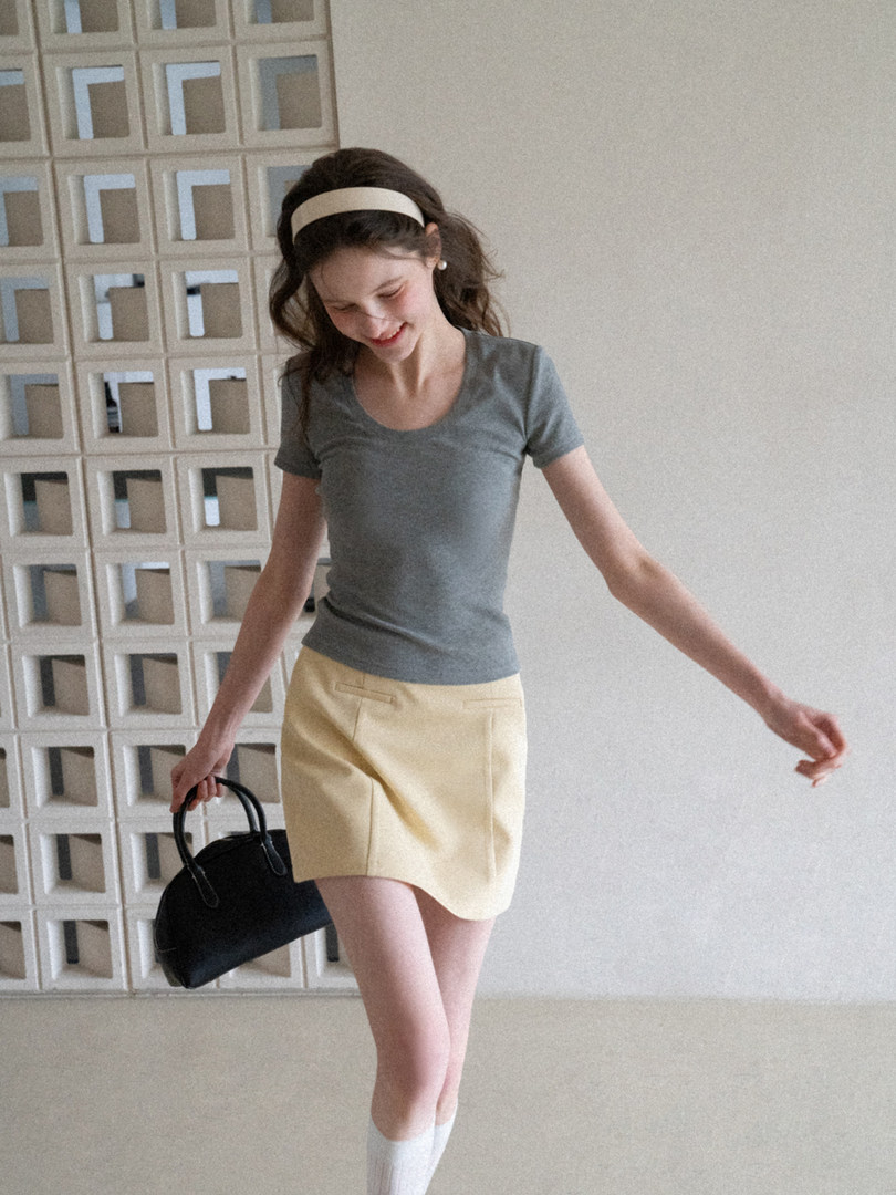 Woman wearing a gray fitted T-shirt and pale yellow mini skirt holding a black handbag.