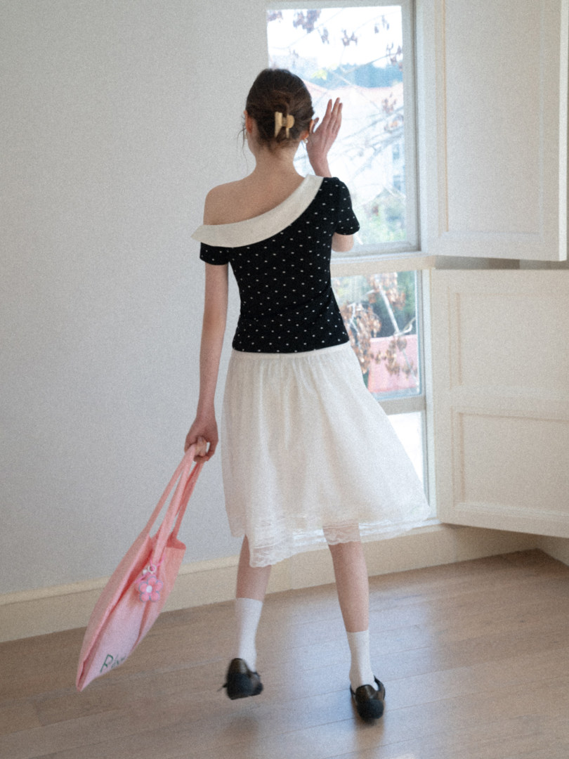 Model wearing a black off-shoulder polka dot top with a white skirt and pink tote bag