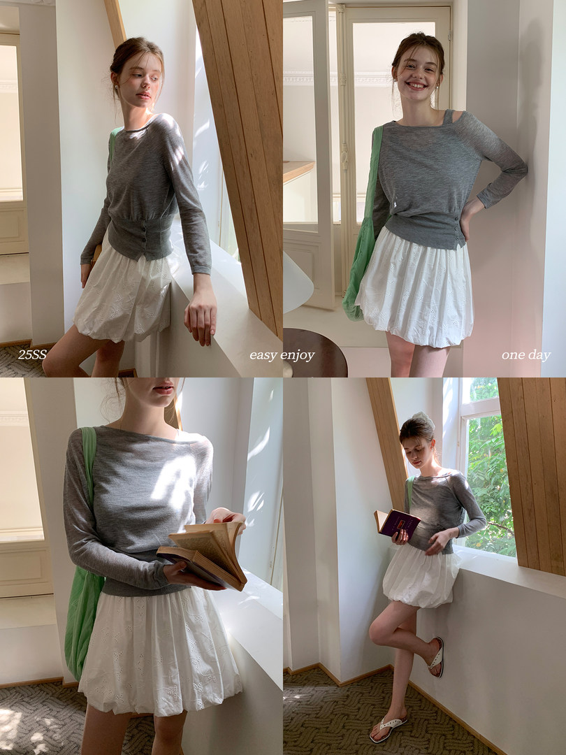 Model wearing a gray long-sleeve top with a white skirt in a bright indoor setting