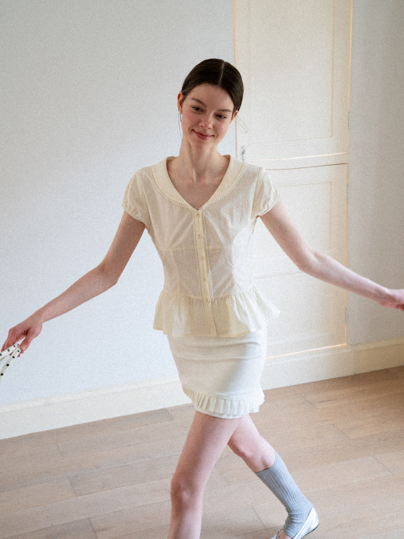 Model wearing a cream short-sleeve buttoned top and matching skirt
