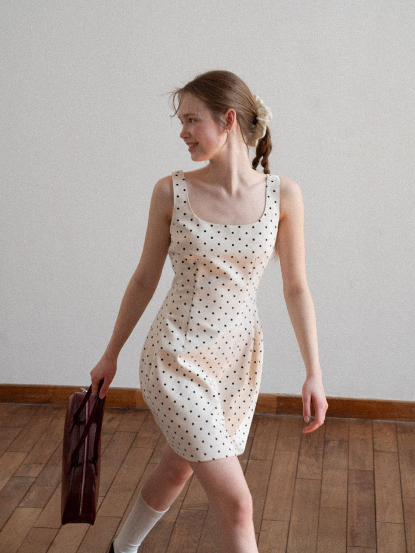 Woman wearing a white polka dot sleeveless mini dress.