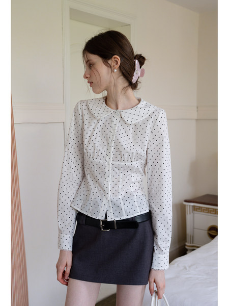 Model wearing a white polka dot long-sleeve blouse with a Peter Pan collar and dark mini skirt