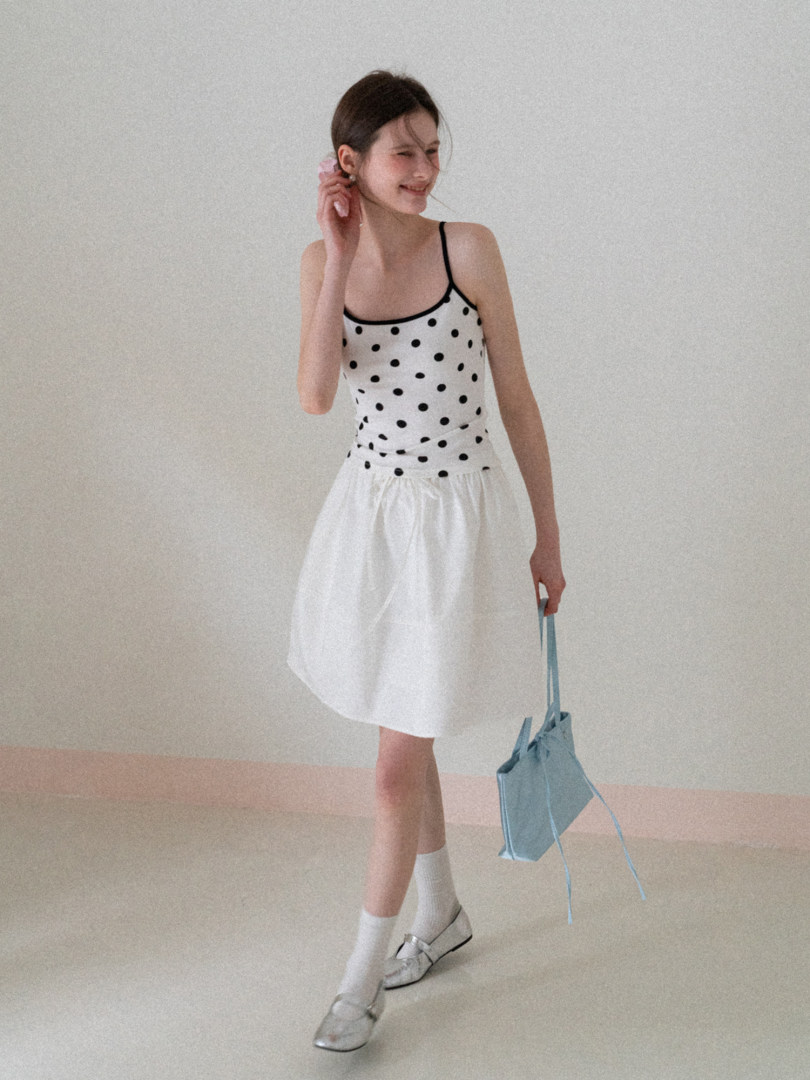Model wearing a white polka dot sleeveless dress with a light blue tote bag