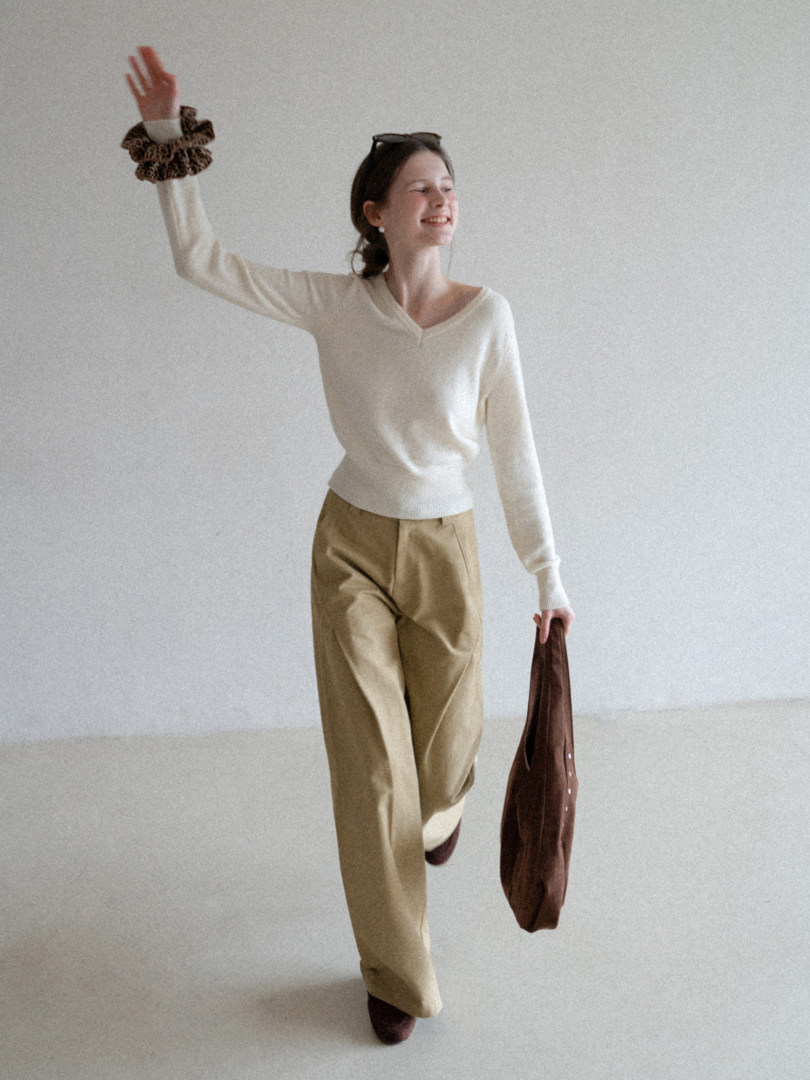 Model wearing a cream sweater with beige trousers and a brown accessory