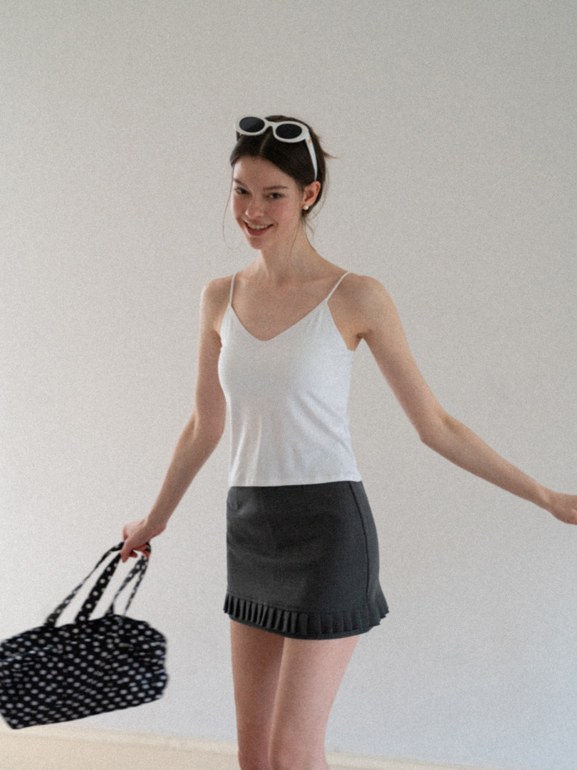 Woman modeling a white camisole top with a dark gray mini skirt and polka dot bag
