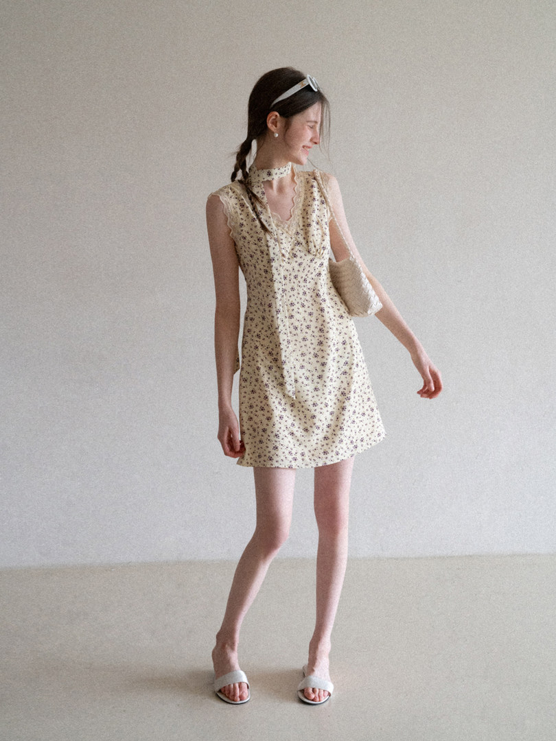 Model wearing a cream floral mini dress with a tie neck and sleeveless design