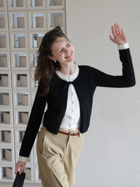 Woman wearing a black cardigan over a white buttoned top with beige trousers.