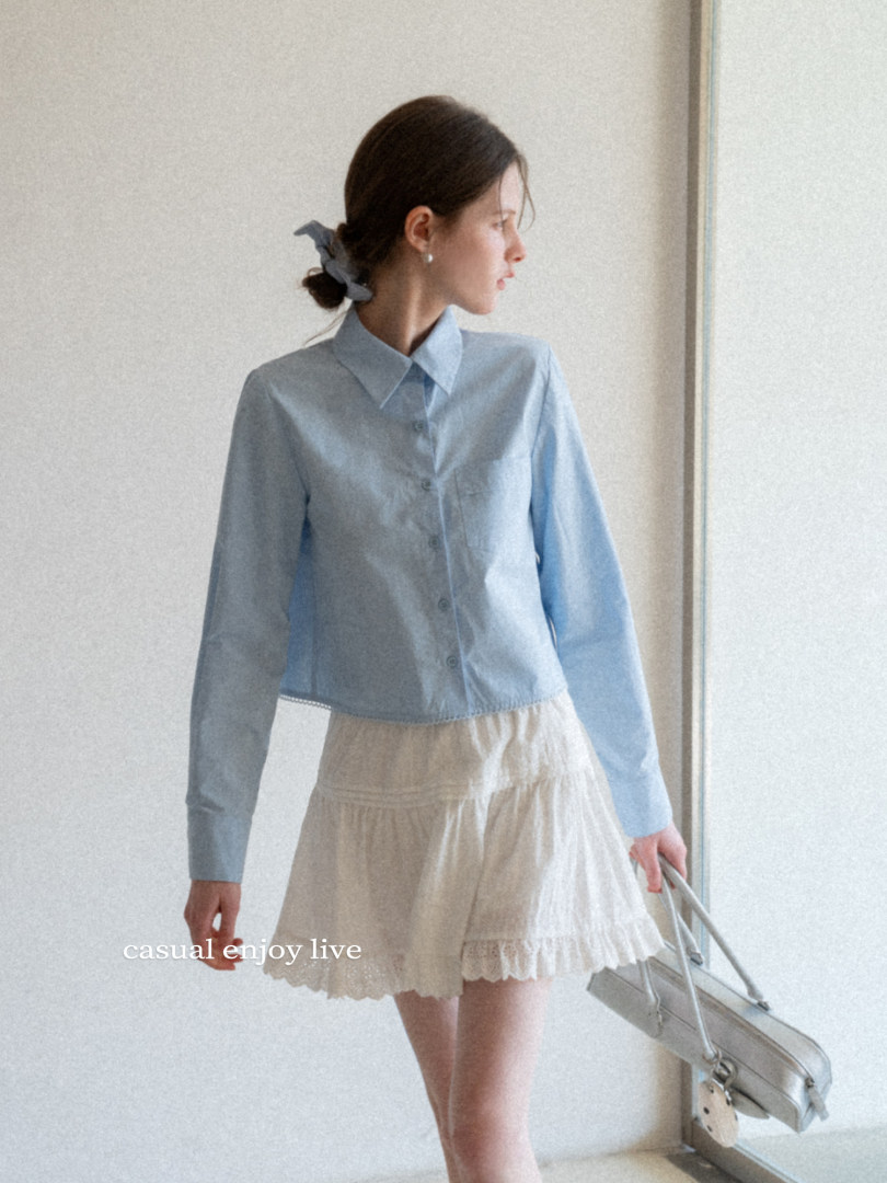 Model wearing a light blue button-up shirt with a cream skirt and handbag