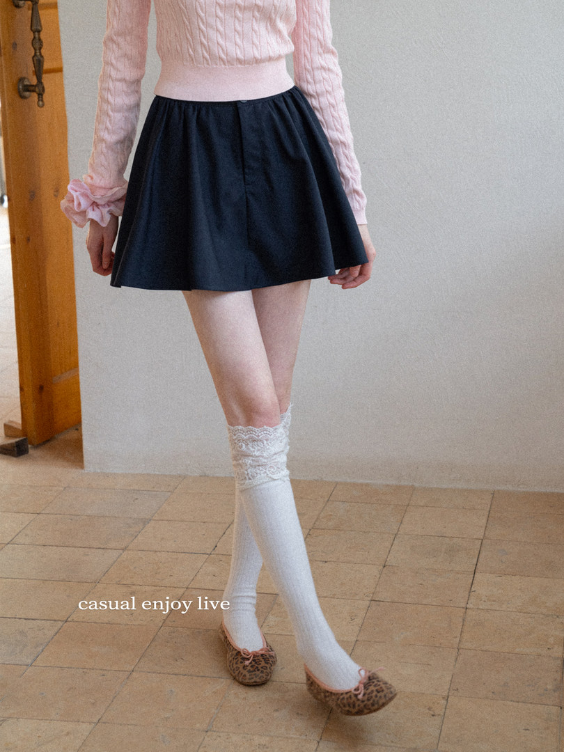 Model wearing a dark pleated mini skirt with a pink cable-knit top