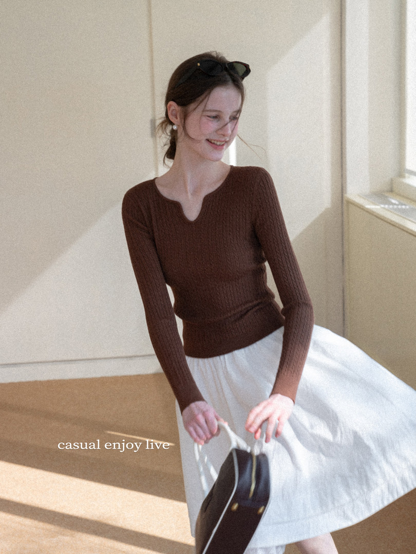 Woman wearing a brown ribbed knit long-sleeve top with a white skirt indoors