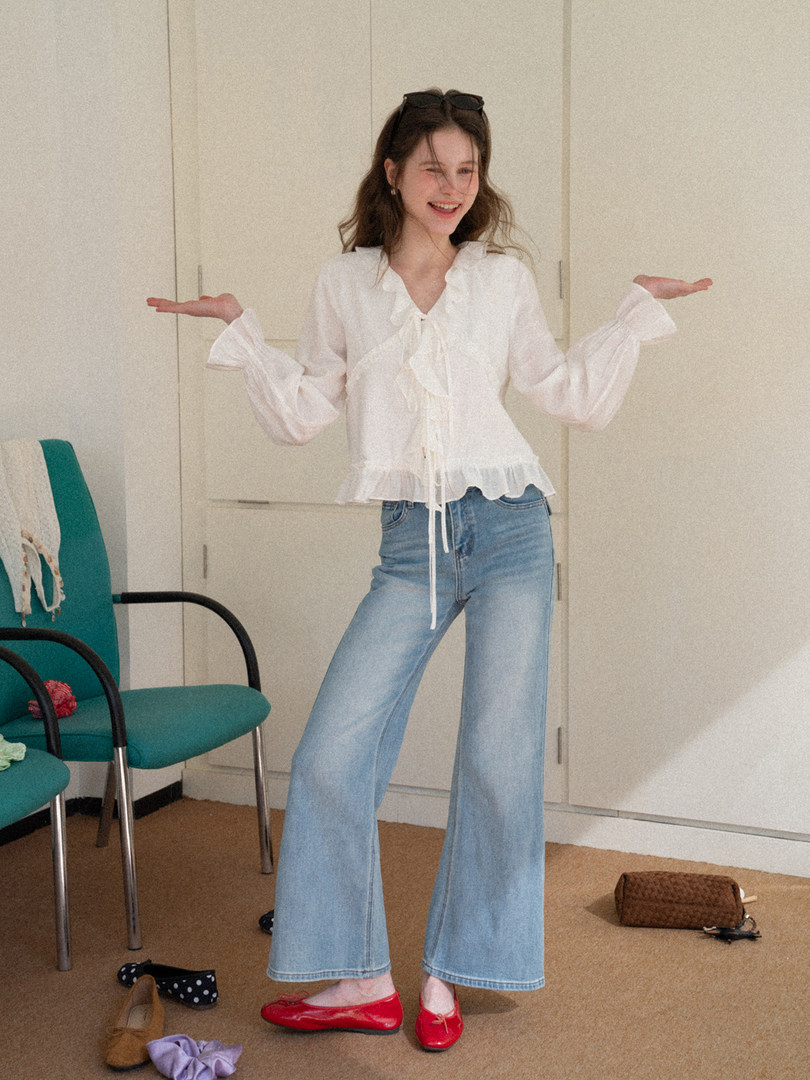 Woman modeling a white ruffled blouse with light blue flared jeans and red flats