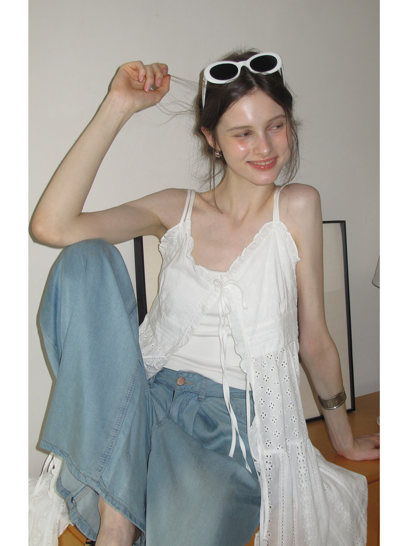 Model wearing a white ruffled eyelet camisole with light blue jeans