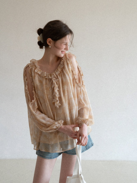Model wearing a sheer ruffled beige blouse with long sleeves