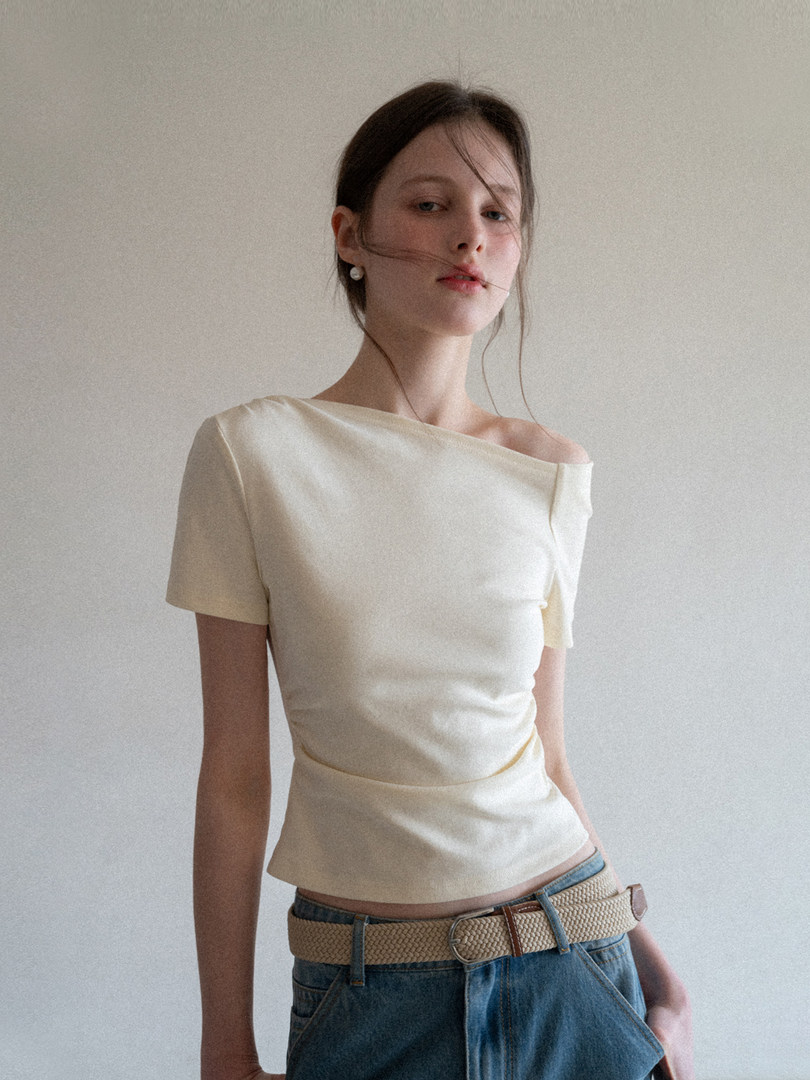 Cream off-shoulder top worn by a model with jeans and a woven belt