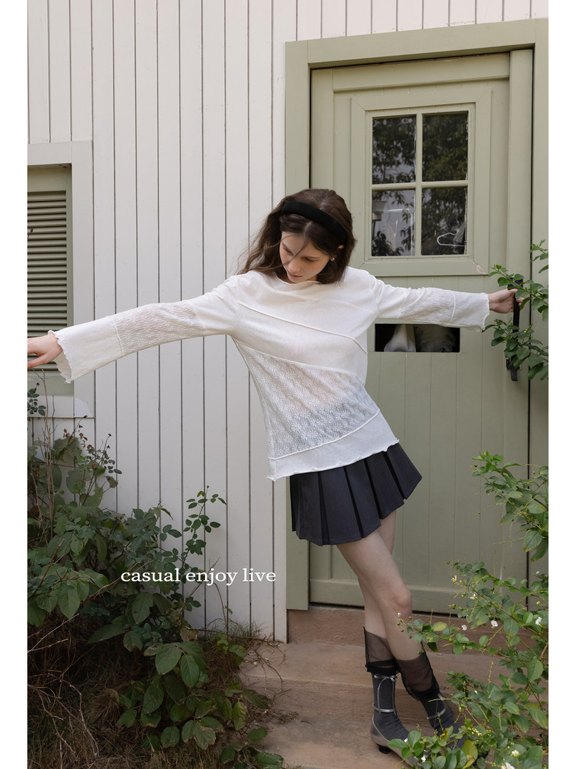 Model wearing a white long-sleeve top with a black pleated skirt outdoors