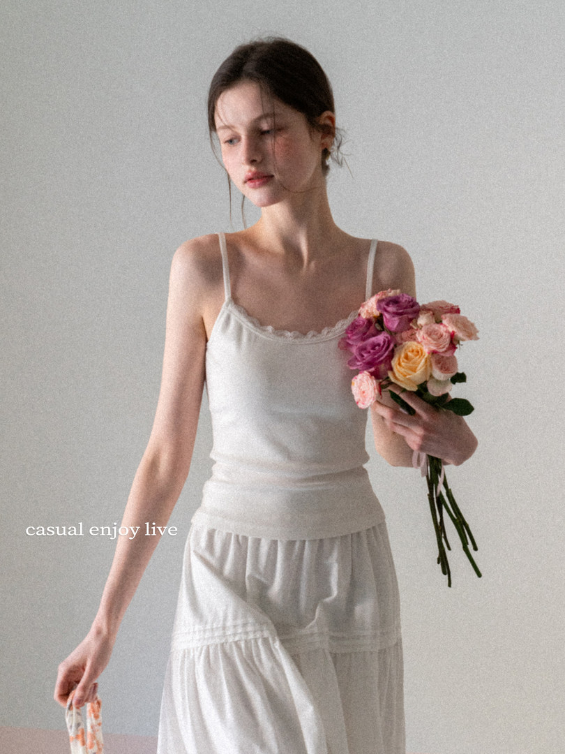 Model wearing a white camisole and skirt while holding a bouquet of flowers