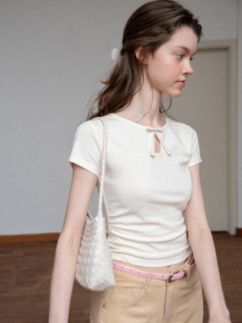Woman wearing a fitted cream short-sleeve top with a small bow detail