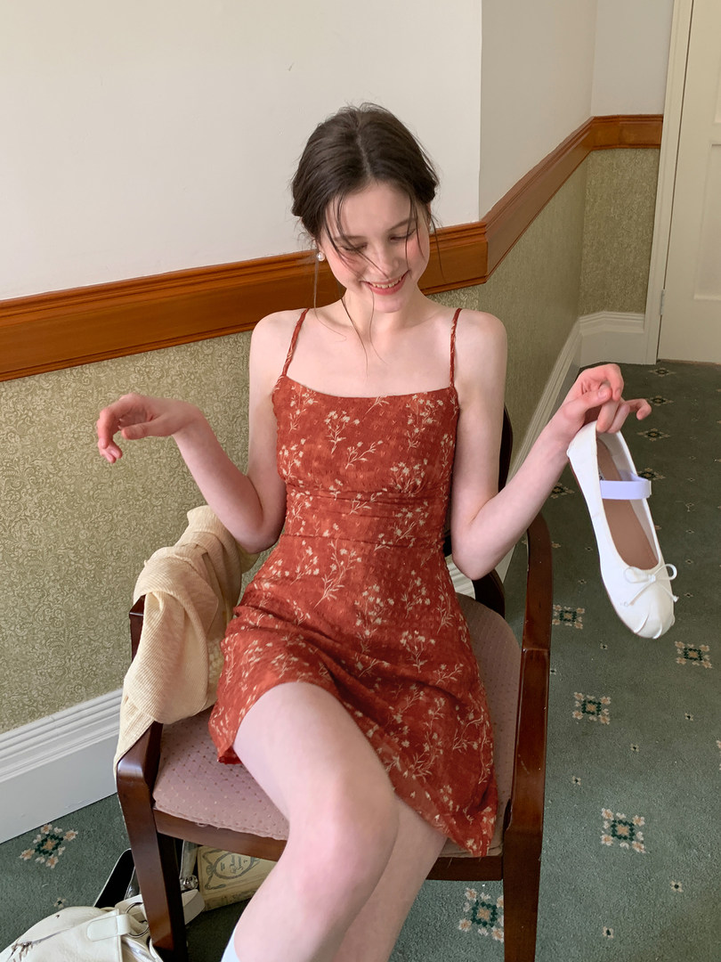 Model wearing a rust floral spaghetti-strap dress while holding white flats
