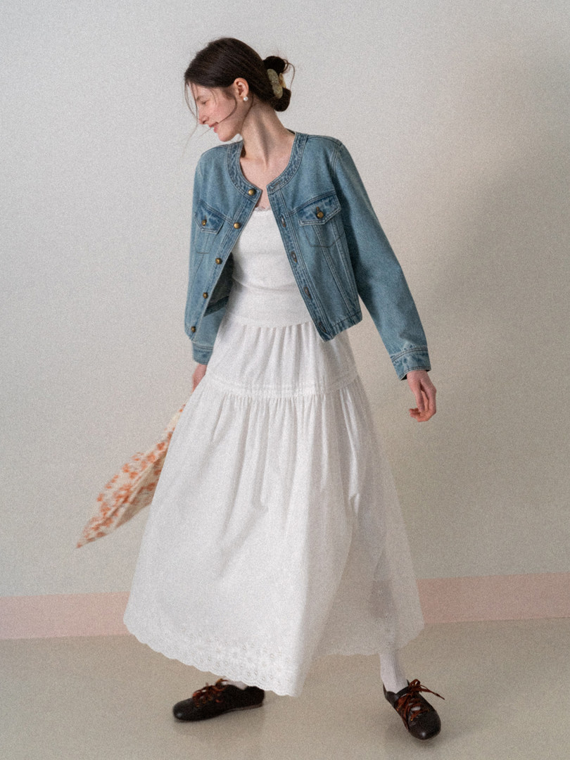 Woman wearing a light blue denim jacket over a white maxi dress