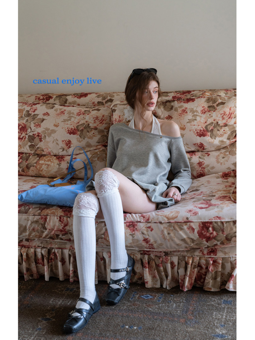 Woman wearing a gray off-shoulder top with white lace socks and black flats on a floral sofa