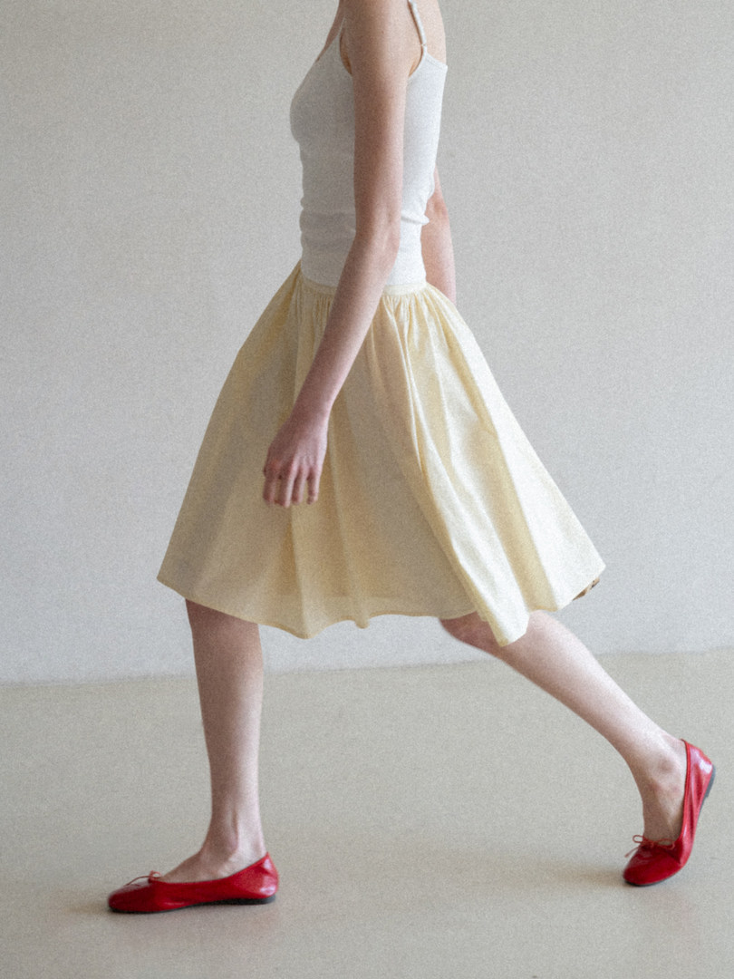 Model wearing a white tank top, pale yellow skirt, and red flats