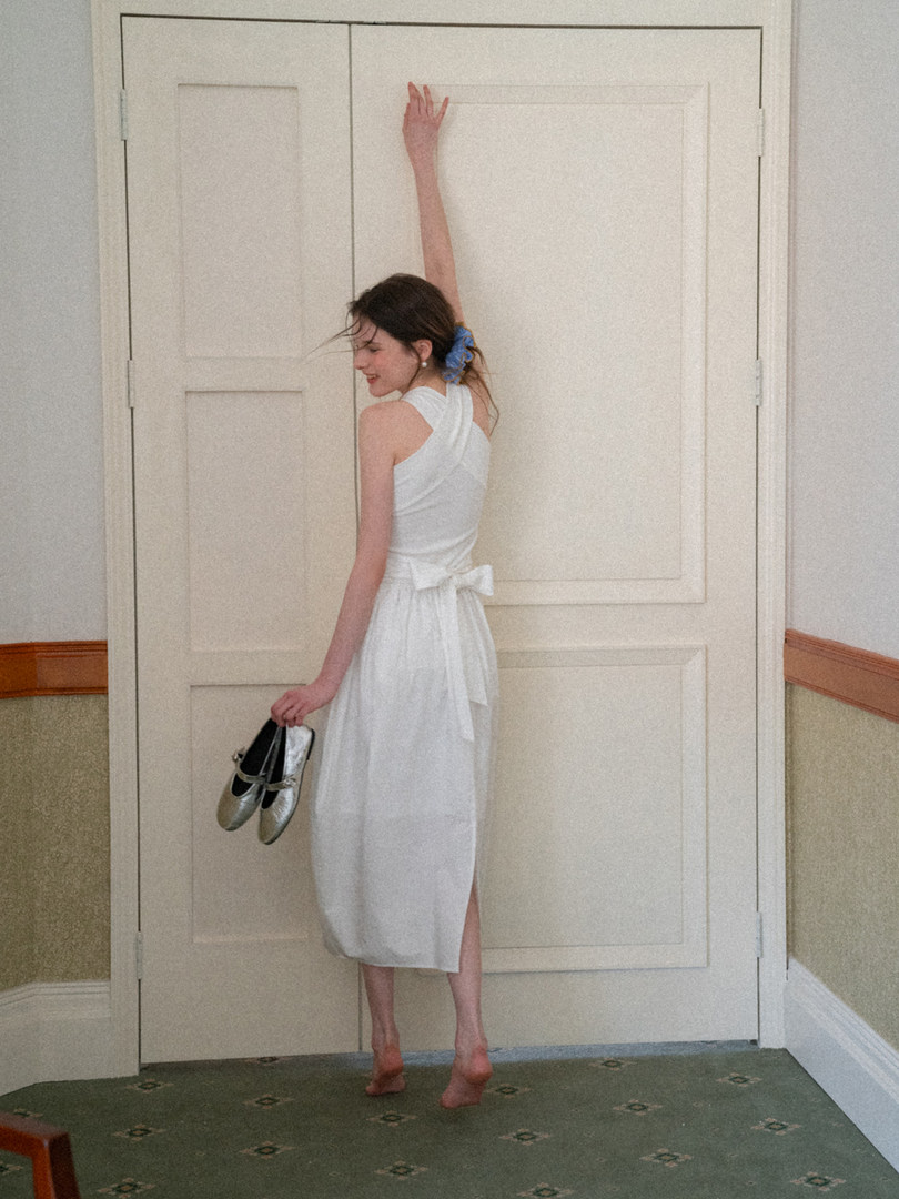 Woman wearing a white sleeveless midi dress with a back bow detail