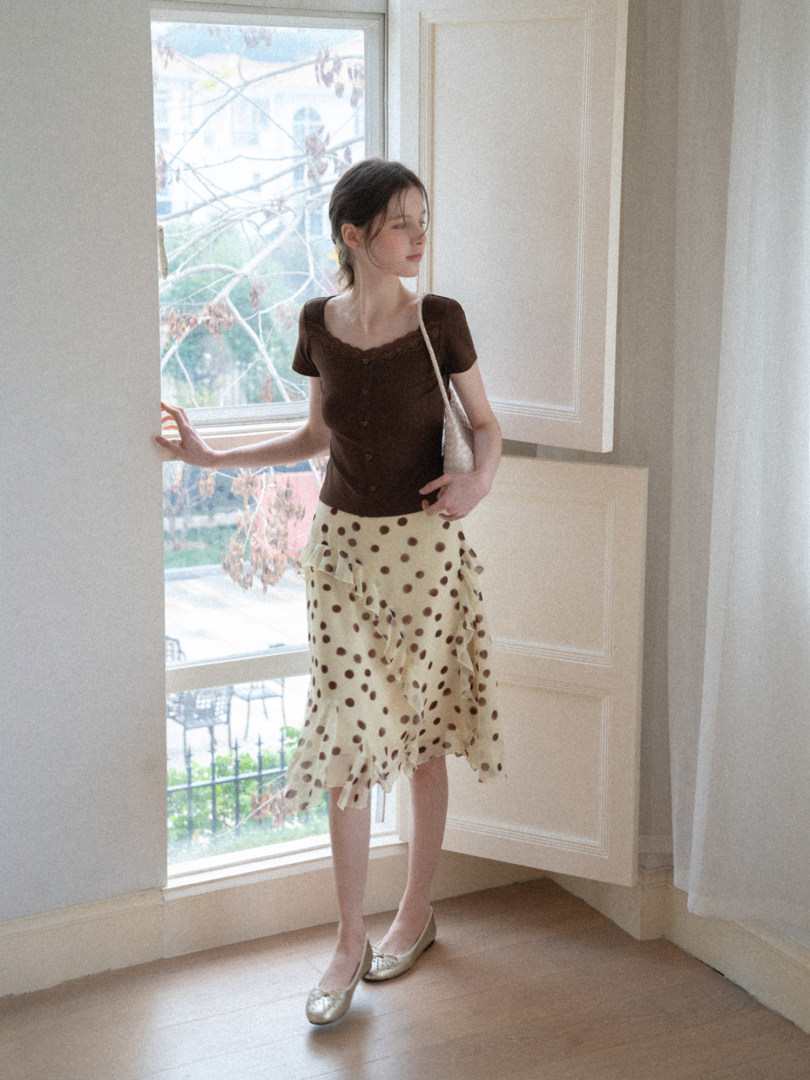 Model wearing a brown short-sleeve top with a cream polka-dot ruffled skirt and flats