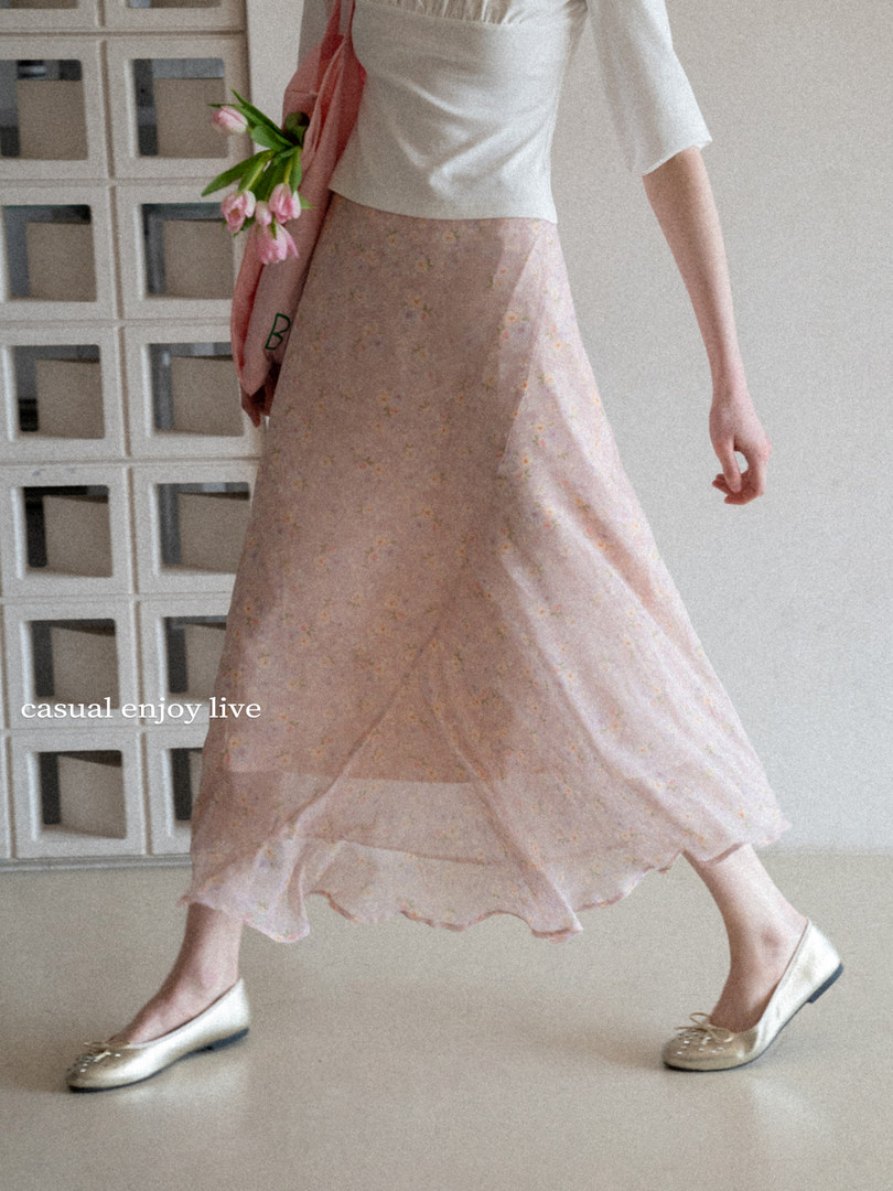 Model wearing a white top with a flowing pink floral skirt and flats