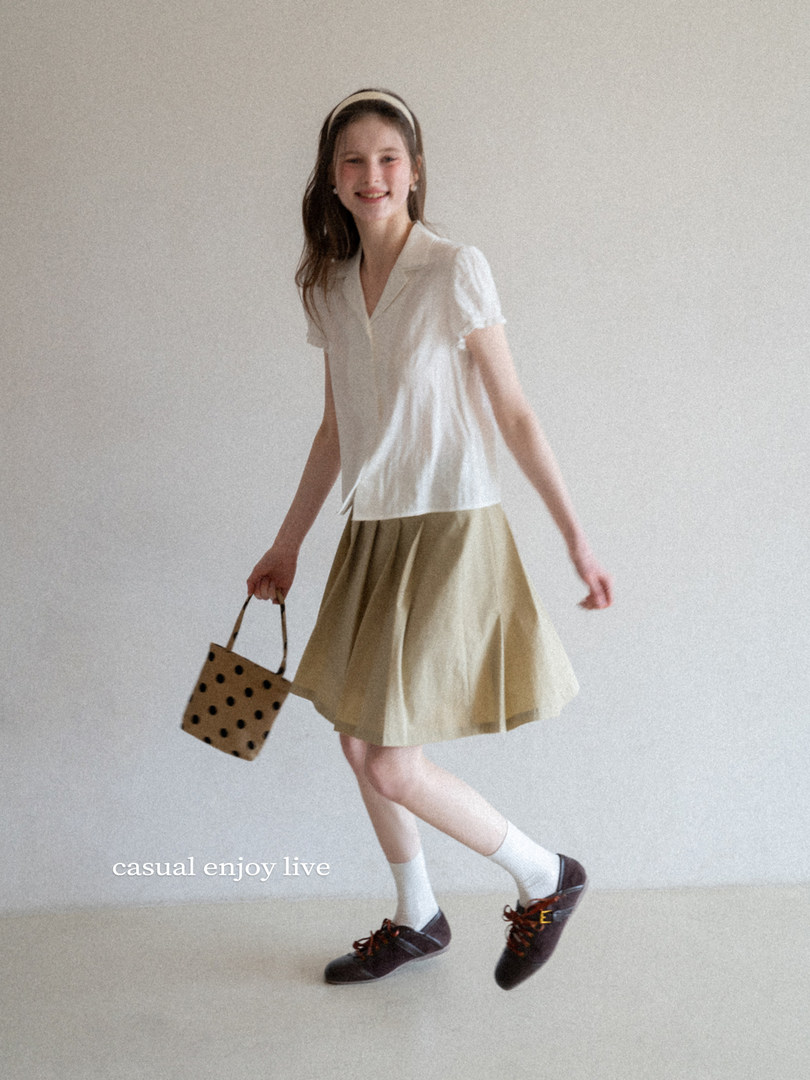 Model wearing a white short-sleeve blouse with a beige skirt and dark lace-up shoes
